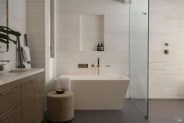 full bath featuring vanity, tile patterned flooring, a freestanding tub, and tile walls