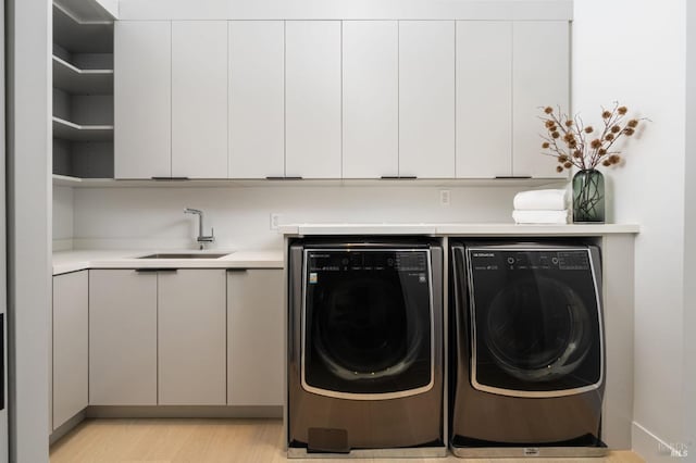 washroom with independent washer and dryer, a sink, cabinet space, and light wood-style floors