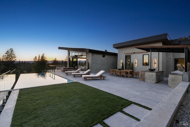 rear view of house featuring stucco siding, a patio, fence, and a lawn
