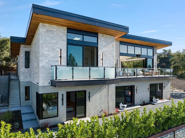 rear view of house featuring a balcony, stone siding, and stucco siding