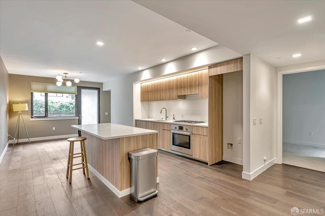 kitchen featuring appliances with stainless steel finishes, light wood-type flooring, a center island, and a notable chandelier