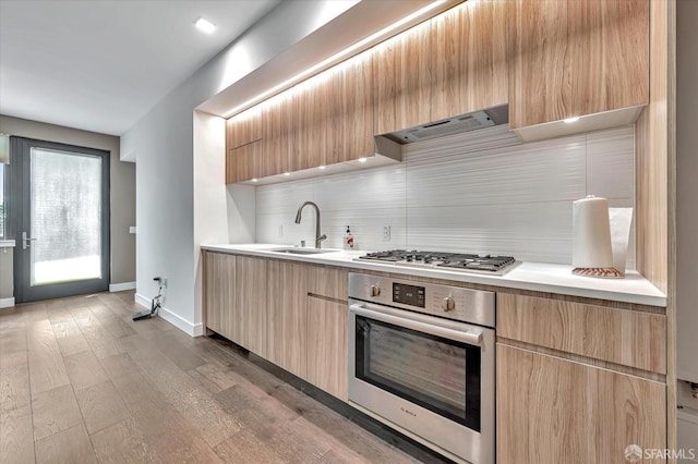 kitchen with sink, light hardwood / wood-style flooring, appliances with stainless steel finishes, extractor fan, and light brown cabinetry