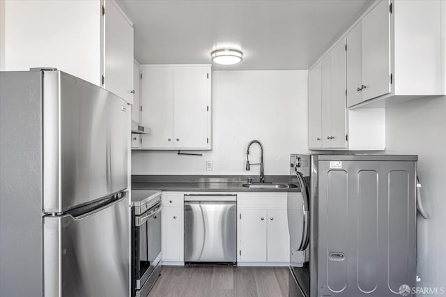 kitchen featuring stainless steel appliances, a sink, white cabinetry, washer / clothes dryer, and dark countertops