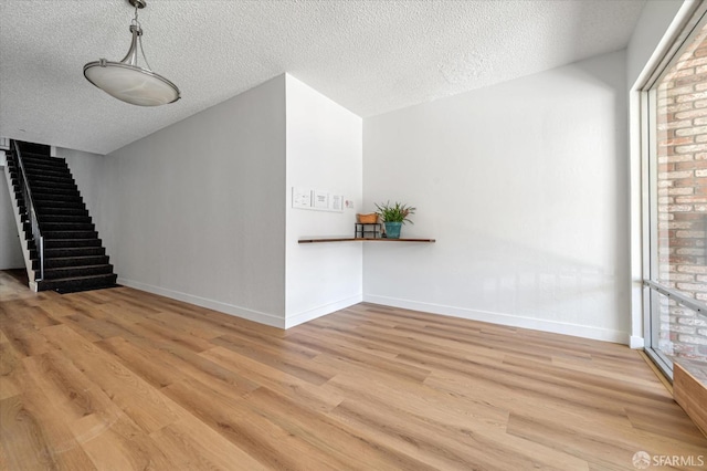 unfurnished living room with stairway, light wood-style flooring, and baseboards