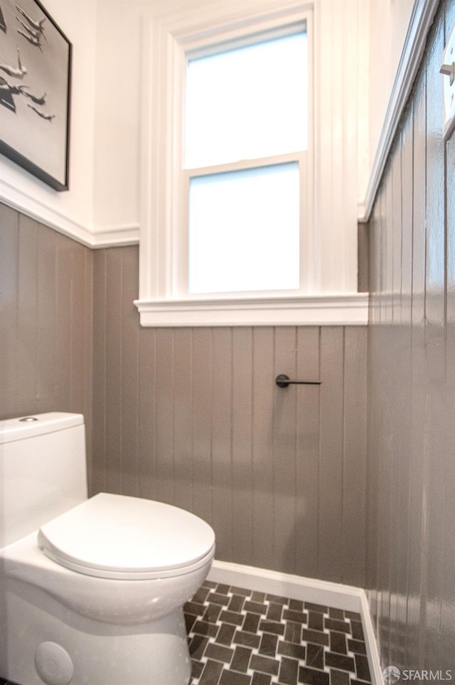 half bath with toilet, wainscoting, and wood walls