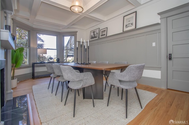 dining room with light wood-style floors, coffered ceiling, beamed ceiling, and a decorative wall
