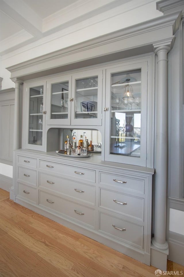 indoor dry bar featuring decorative columns and light wood-style floors