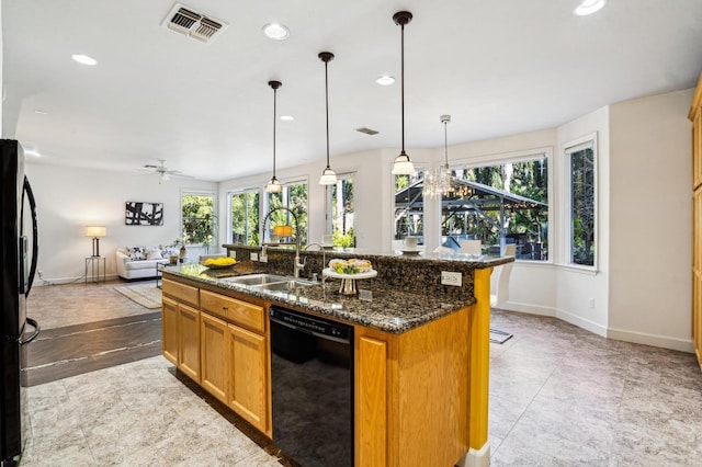 kitchen featuring black appliances, sink, pendant lighting, dark stone counters, and a center island with sink