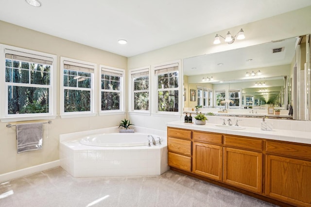 bathroom with a healthy amount of sunlight, a relaxing tiled tub, and vanity