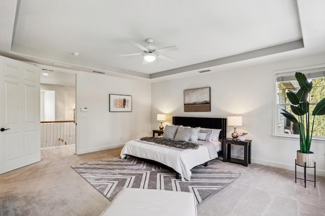 carpeted bedroom with ceiling fan and a raised ceiling