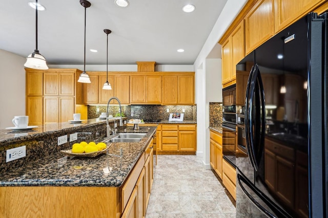 kitchen featuring a kitchen island with sink, sink, black fridge, pendant lighting, and backsplash