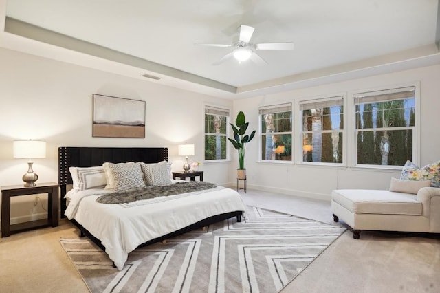 bedroom with ceiling fan, a tray ceiling, and light carpet