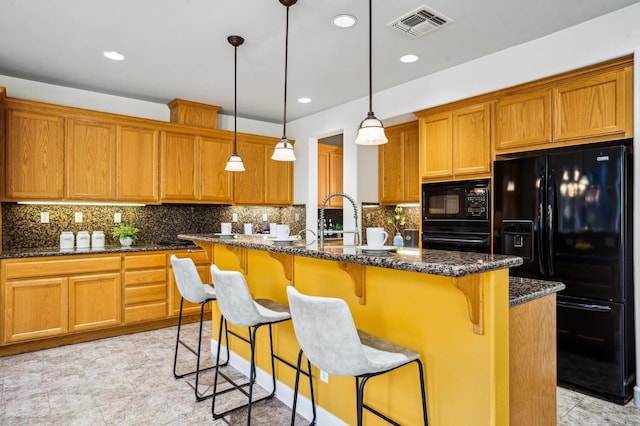 kitchen with black appliances, dark stone counters, and an island with sink