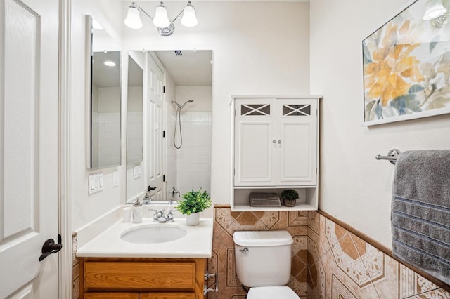 bathroom with tile walls, toilet, vanity, and a tile shower