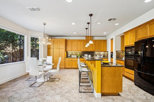 kitchen with black appliances, hanging light fixtures, a kitchen breakfast bar, dark stone countertops, and a center island with sink