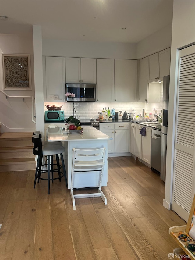 kitchen with white cabinets, backsplash, stainless steel appliances, and light hardwood / wood-style floors