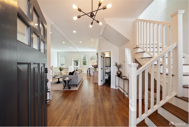 entrance foyer with dark wood-style floors, stairs, crown molding, and an inviting chandelier