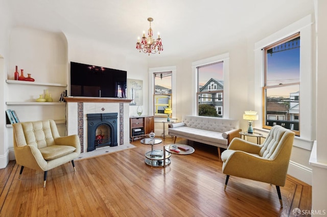 living room with hardwood / wood-style flooring, a tiled fireplace, and an inviting chandelier