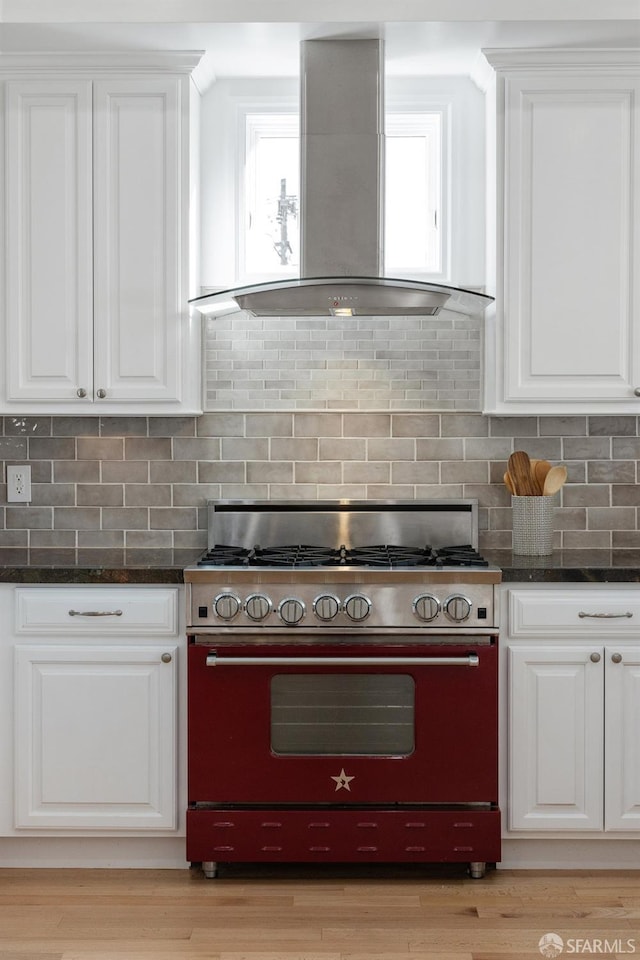 kitchen with dark stone countertops, white cabinets, wall chimney exhaust hood, and stove