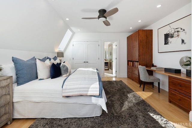 bedroom with built in desk, light hardwood / wood-style floors, a closet, and vaulted ceiling