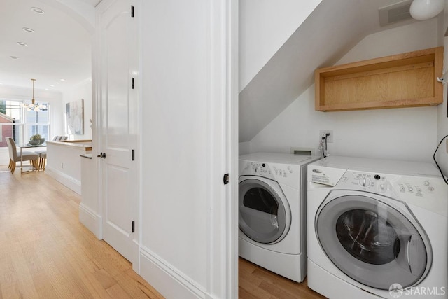 clothes washing area featuring an inviting chandelier, independent washer and dryer, and light hardwood / wood-style flooring