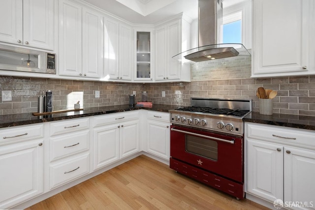 kitchen with stainless steel microwave, white cabinetry, dark stone countertops, exhaust hood, and range