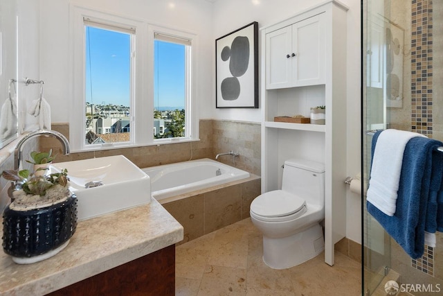 bathroom with vanity, tiled tub, and toilet