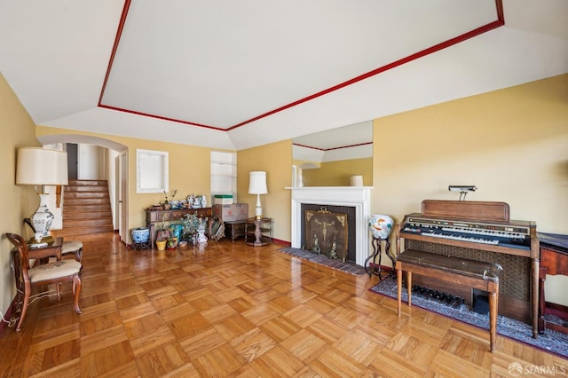 living room featuring arched walkways, a tile fireplace, lofted ceiling, and stairs