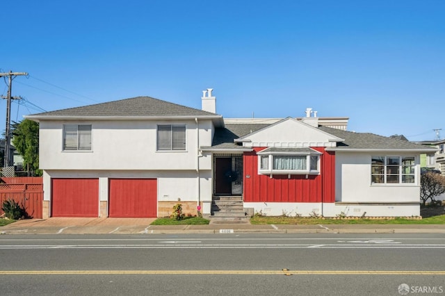 split level home with a garage, fence, concrete driveway, roof with shingles, and a chimney