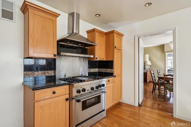 kitchen featuring wall chimney range hood, visible vents, backsplash, and stainless steel stove