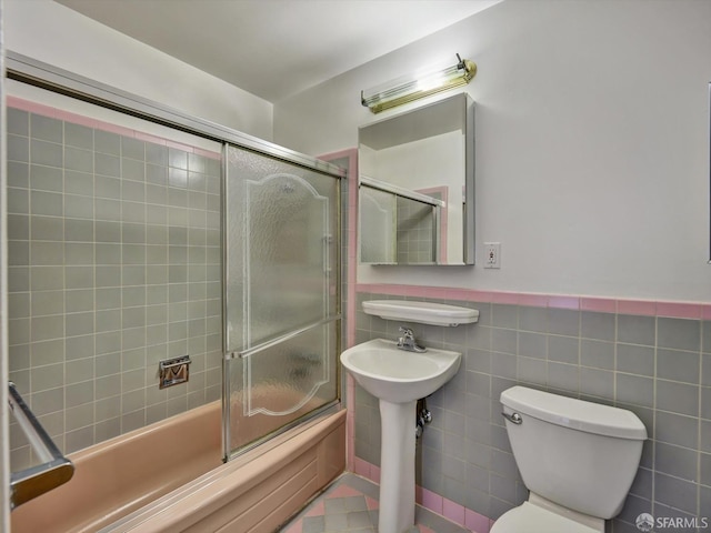 bathroom featuring enclosed tub / shower combo, toilet, and tile walls