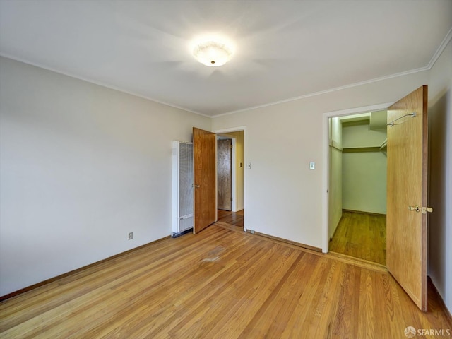 unfurnished bedroom with a spacious closet, light hardwood / wood-style flooring, ornamental molding, and a closet