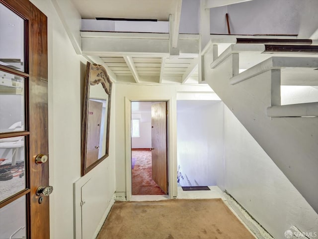 hall with beamed ceiling and light colored carpet