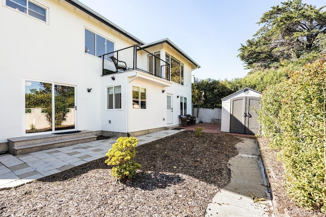 back of house with a patio, stucco siding, a storage unit, a balcony, and an outdoor structure