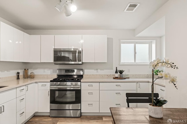 kitchen featuring light wood finished floors, stainless steel appliances, light countertops, visible vents, and white cabinets