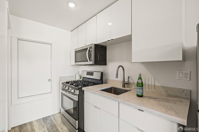 kitchen with light stone counters, stainless steel appliances, a sink, white cabinets, and light wood-style floors