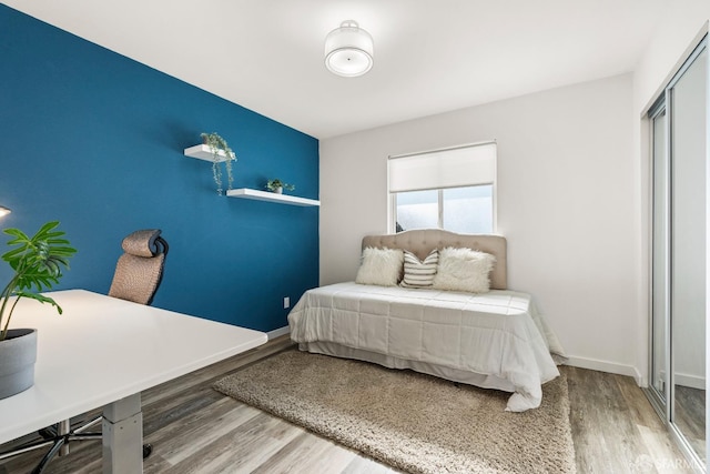 bedroom featuring an accent wall, wood finished floors, and baseboards