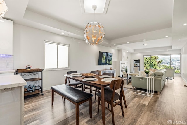 dining room with a notable chandelier, light wood finished floors, recessed lighting, a raised ceiling, and baseboards