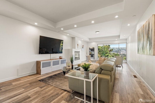 living room featuring a tray ceiling, recessed lighting, baseboards, and wood finished floors