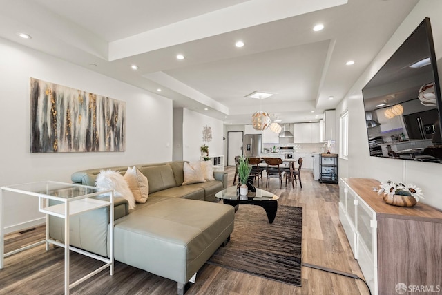 living room featuring light wood finished floors, a tray ceiling, visible vents, and recessed lighting