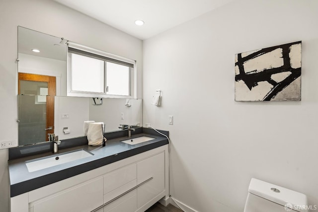 bathroom with double vanity, a sink, toilet, and recessed lighting