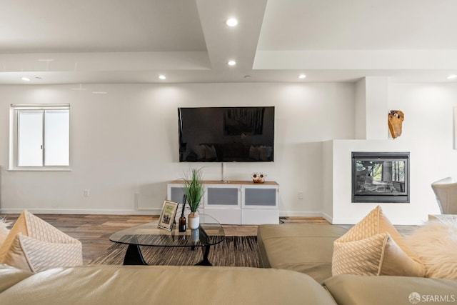 living area featuring recessed lighting, a glass covered fireplace, wood finished floors, baseboards, and a raised ceiling