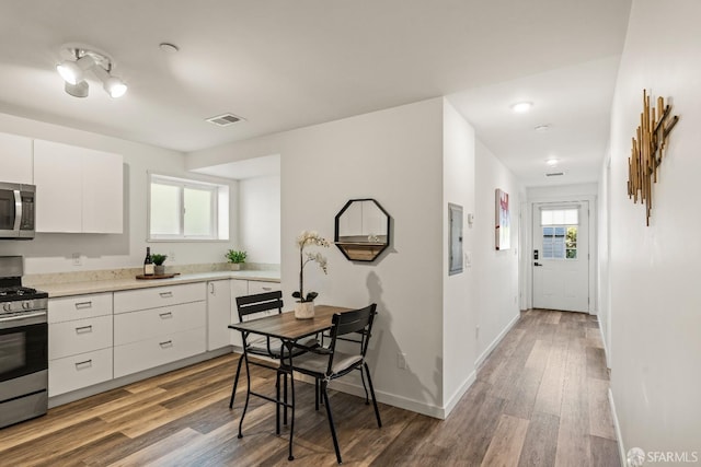 kitchen featuring stainless steel appliances, wood finished floors, visible vents, baseboards, and white cabinets