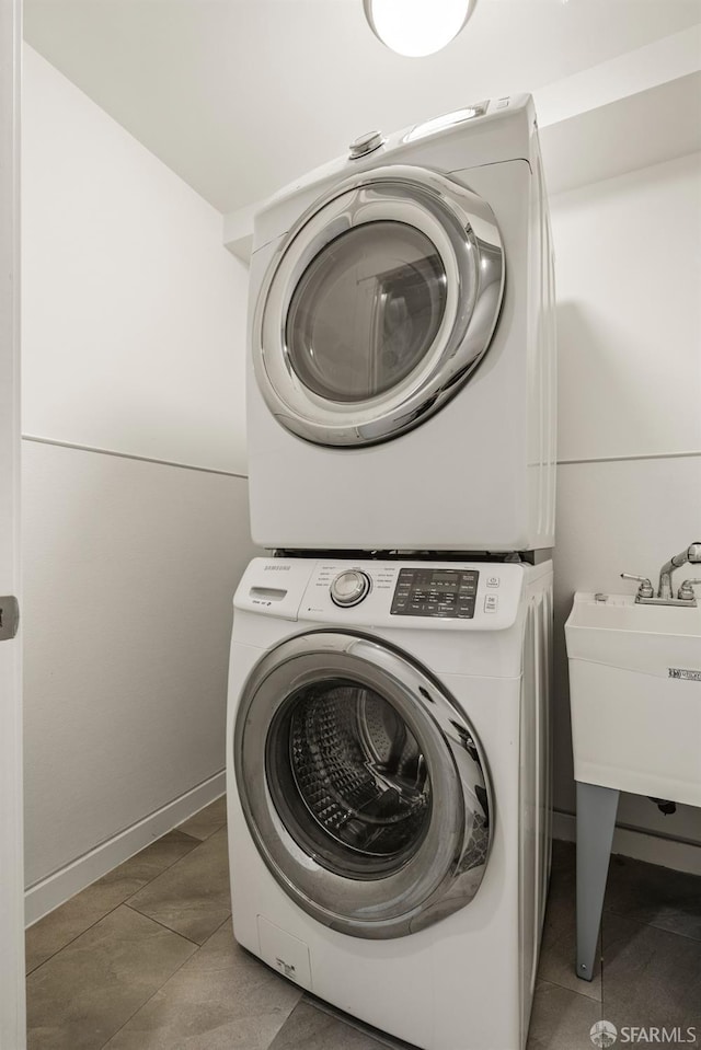 laundry area with laundry area, light tile patterned flooring, a sink, and stacked washer and clothes dryer