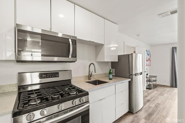 kitchen with visible vents, appliances with stainless steel finishes, white cabinets, a sink, and light wood-type flooring