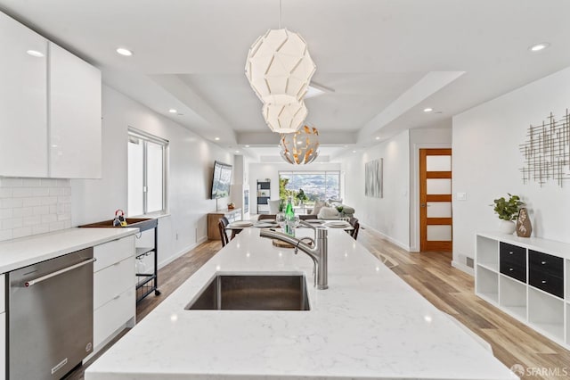 kitchen featuring modern cabinets, open floor plan, a tray ceiling, stainless steel dishwasher, and a sink