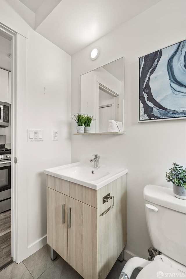 half bath featuring tile patterned flooring, vanity, toilet, and baseboards