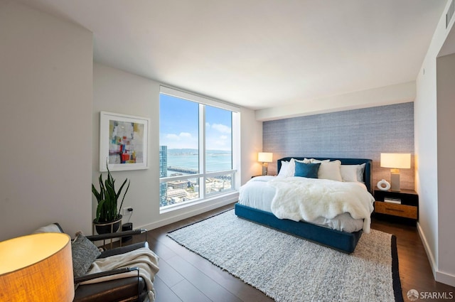 bedroom with dark hardwood / wood-style flooring and a water view