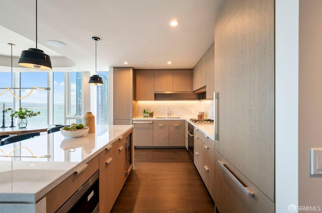 kitchen featuring light brown cabinets, dark hardwood / wood-style floors, stainless steel gas cooktop, oven, and pendant lighting