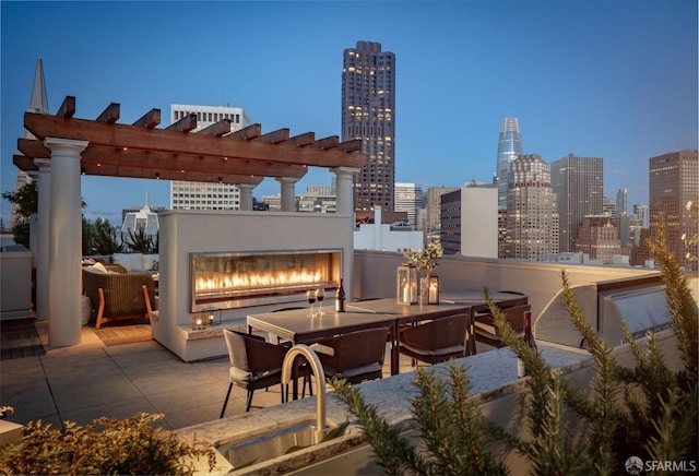 patio terrace at dusk with a pergola, sink, and exterior fireplace